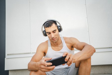 Photo for Portrait of young man outdoor use headphones and smart phone to play video games - Royalty Free Image