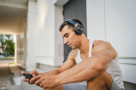 Foto de Retrato de hombre joven al aire libre uso de auriculares y teléfono inteligente para jugar videojuegos - Imagen libre de derechos
