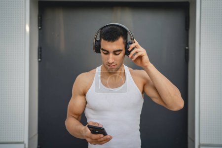 Téléchargez les photos : Portrait de jeune homme en plein air utiliser des écouteurs et un téléphone intelligent pour jouer de la musique ou regarder un podcast vidéo - en image libre de droit