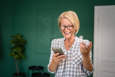 Téléchargez les photos : Une femme mature caucasienne blonde femme utiliser téléphone mobile smartphone pour envoyer des messages texte sms seul heureux confiant vraies personnes copier l'espace - en image libre de droit