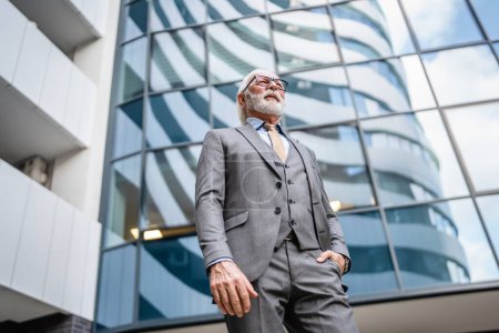 Photo for Portrait of senior man with beard businessman in suit stand outdoor in front of modern building corporation real person copy space - Royalty Free Image