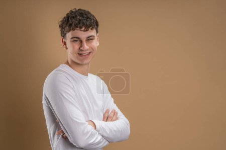 Téléchargez les photos : Portrait d'un homme caucasien de 20 ans regardant vers l'appareil photo en face de couleur amande studio arrière-plan souriant portant casual shirt copie espace - en image libre de droit