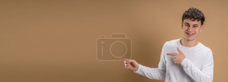 Téléchargez les photos : Portrait d'un homme caucasien de 20 ans regardant vers l'appareil photo en face de couleur amande studio arrière-plan souriant portant casual point de chemise sur l'espace de copie - en image libre de droit