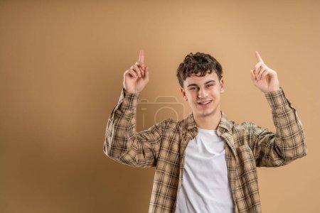 Téléchargez les photos : Portrait d'un homme caucasien de 20 ans regardant vers l'appareil photo en face de couleur amande studio arrière-plan souriant portant casual point de chemise sur l'espace de copie - en image libre de droit