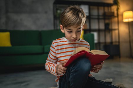 Téléchargez les photos : Un garçon caucasien à la maison a lu un livre dans la vue du soir espace de copie concept d'éducation des personnes réelles - en image libre de droit