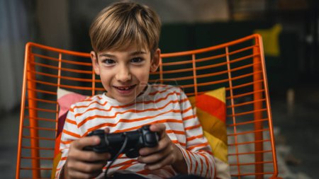 Foto de Un niño se sienta en casa mantenga joystick controlador jugar videojuegos consola - Imagen libre de derechos