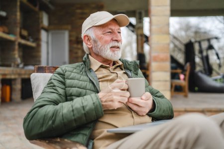 Foto de Un hombre mayor se sienta al aire libre en otoño día mantenga taza de café o té - Imagen libre de derechos