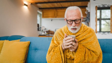 Téléchargez les photos : Un homme âgé caucasien assis sur le canapé-lit à la maison tenir tasse de thé froid commun éternuer malade attrapé froid - en image libre de droit