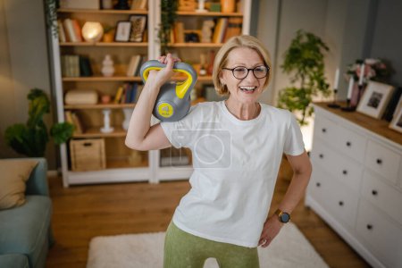 Una mujer rubia caucásica madura entrenando con kettlebell girya campana rusa en casa ejercicio femenino en su apartamento concepto de estilo de vida saludable