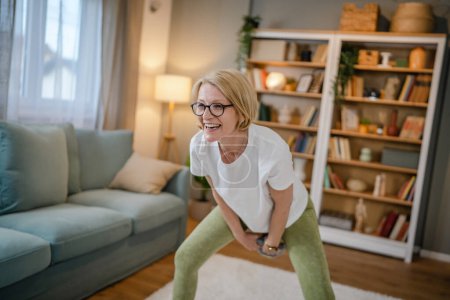 Eine reife kaukasische Blondine trainiert mit Kettlebell girya russische Glocke zu Hause weibliche Bewegung in ihrer Wohnung gesundes Lebensstilkonzept