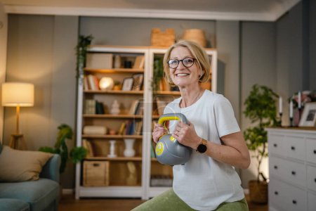 Una mujer rubia caucásica madura entrenando con kettlebell girya campana rusa en casa ejercicio femenino en su apartamento concepto de estilo de vida saludable