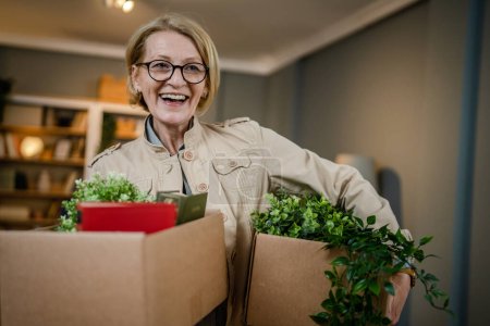 Photo for One senior woman pensioner grandmother moving in new apartment taking her stuff belongings and plants in or out of boxes packing or unpacking real person copy space - Royalty Free Image