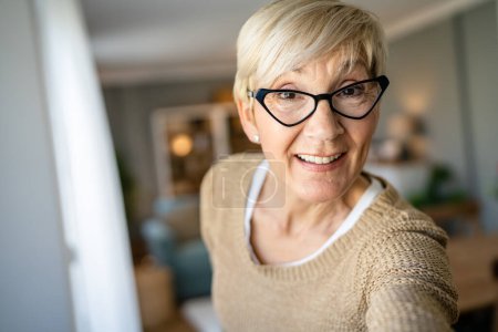 Téléchargez les photos : Gros plan portrait d'une femme âgée aux cheveux courts heureux sourire positif émotion copie espace debout à la maison porter des lunettes d'intérieur autoportrait ugc utilisateur généré contenu - en image libre de droit