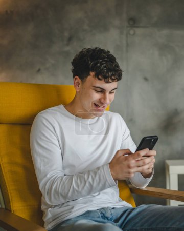Foto de Un hombre caucásico varón adolescente uso teléfono móvil smartphone para la navegación en línea de Internet red social o mensajes de texto SMS en casa - Imagen libre de derechos