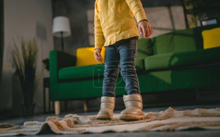 Foto de Girl toddler child puts on her own boots in the winter at home - Imagen libre de derechos