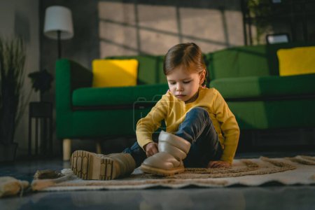 Photo for Girl toddler child puts on her own boots in the winter at home - Royalty Free Image