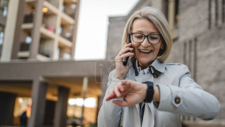 Photo for One modern woman mature female stand in the city outdoor use mobile phone send text messages sms or browse internet online blonde female with eyeglasses copy space - Royalty Free Image