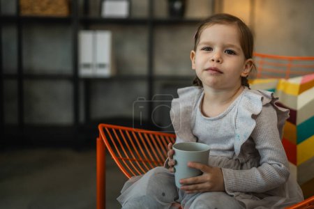 Foto de Un niño pequeño niña caucásica niño sostiene vaso de bebida de agua en casa - Imagen libre de derechos