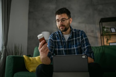 Téléchargez les photos : One man hold medicine drugs bottle pills read label on digital tablet - en image libre de droit