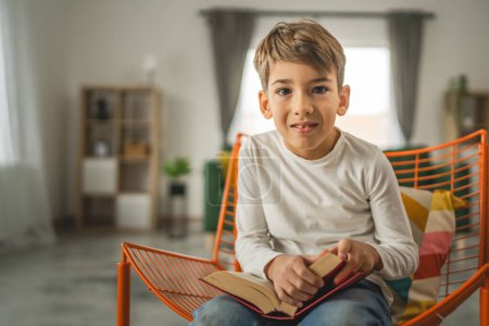 Téléchargez les photos : Un garçon enfant caucasien de sept ans enfant dans la chambre à la maison lire le livre - en image libre de droit