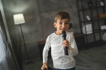 Téléchargez les photos : Garçon sept ans enfant tenir microphone à la maison heureux sourire chanter - en image libre de droit
