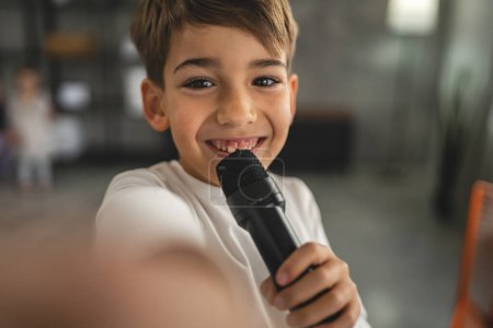 Téléchargez les photos : Garçon sept ans enfant tenir microphone à la maison heureux sourire chanter - en image libre de droit