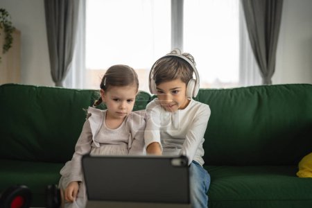 Foto de Hermano y hermana niños pequeños hermanos usan tableta digital en casa ver video en línea - Imagen libre de derechos