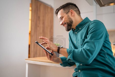 Photo for One man adult caucasian male hold a digital tablet work or browse internet happy smile at home sit confident daily morning routine copy space real person - Royalty Free Image