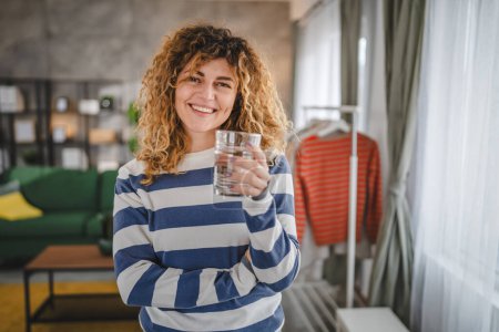 Foto de Una mujer hermosa hembra adulta en casa con vaso de agua pelo rizado sonrisa feliz estilo de vida saludable concepto de hidratación - Imagen libre de derechos