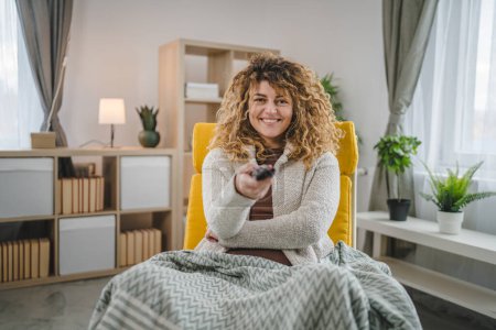 Foto de Una mujer se sienta en casa con mando a distancia ver TV sonrisa feliz - Imagen libre de derechos