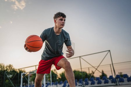 Foto de Un adolescente caucásico hombre caucásico joven de pie en la cancha de baloncesto con pelota en la noche listo para jugar espacio de copia juego persona real - Imagen libre de derechos