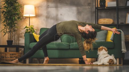 Foto de La mujer practica yoga en la estera en la sala de estar en casa - Imagen libre de derechos