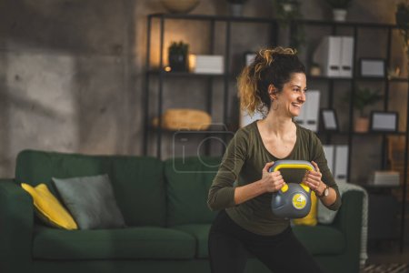 Foto de Una mujer adulta entrenando en casa uso kettlebell girya peso - Imagen libre de derechos