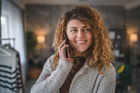 Téléchargez les photos : Une femme caucasienne adulte femelle avec des cheveux bouclés à la maison utiliser téléphone mobile pour faire un appel parler heureux sourire copie espace - en image libre de droit