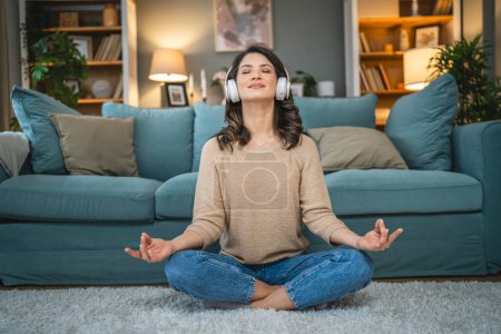 Téléchargez les photos : Une femme adulte caucasien femelle millénium en utilisant des écouteurs pour la méditation guidée en ligne pratiquant le yoga pleine conscience à la maison personnes réelles espace de copie concept d'auto-soins - en image libre de droit