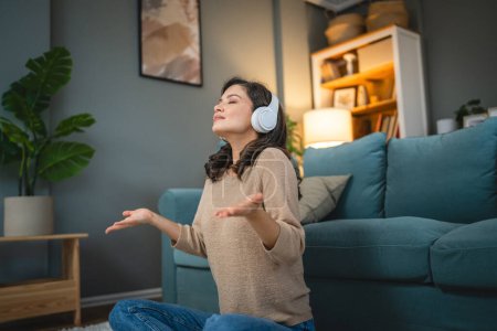Téléchargez les photos : Une femme adulte caucasien femelle millénium en utilisant des écouteurs pour la méditation guidée en ligne pratiquant le yoga pleine conscience à la maison personnes réelles espace de copie concept d'auto-soins - en image libre de droit
