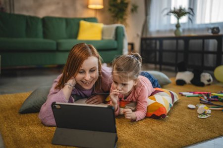 Photo for Mother and daughter use digital tablet to watch online video at home - Royalty Free Image