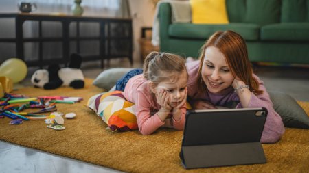 Photo for Mother and daughter use digital tablet to watch online video at home - Royalty Free Image