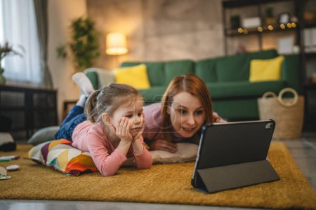 Téléchargez les photos : Mère et fille utilisent une tablette numérique pour regarder une vidéo en ligne à la maison - en image libre de droit