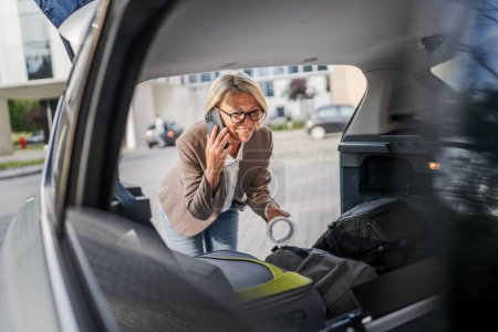 Photo for One mature blonde beautiful business woman travel concept female take stuff belongings from the back of her car while moving or arrive to destination or work make a phone call real people copy space - Royalty Free Image