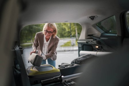 Photo for One mature blonde beautiful business woman travel concept female take stuff belongings from the back of her car while moving or arrive to destination or work real people copy space - Royalty Free Image