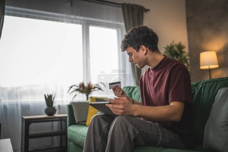 Foto de Un joven adolescente caucásico hombre sentarse en casa uso de la tarjeta de crédito compras en línea uso de Internet para la compra en línea activa moderna e-banca - Imagen libre de derechos