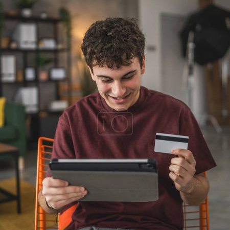 Foto de Un joven adolescente caucásico hombre sentarse en casa uso de la tarjeta de crédito compras en línea uso de Internet para la compra en línea activa moderna e-banca - Imagen libre de derechos
