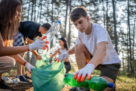 Foto de Grupo de amigos adolescentes gen Z hombres y mujeres caucásicos mujeres recogiendo basura botellas de plástico y papel del bosque limpiando la naturaleza en el concepto de ecología de cuidado ambiental de día soleado - Imagen libre de derechos