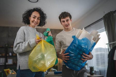 Photo for Mother and son woman and teenage man family recycle at home sorting waste plastic paper and glass to bags sustainable living concept - Royalty Free Image