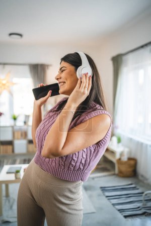 Photo for One caucasian woman adult female with headphones use mobile phone at home to listen to the music online happy smile sing joy have fun alone - Royalty Free Image