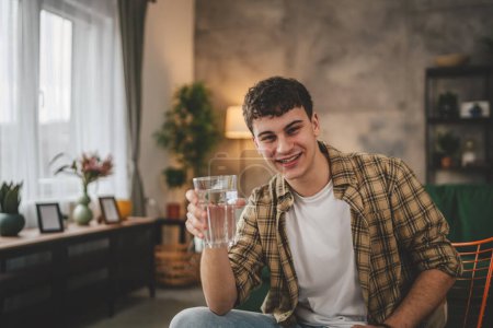 Téléchargez les photos : Portrait de l'homme jeune homme caucasien adolescent tenir verre d'eau à la maison - en image libre de droit