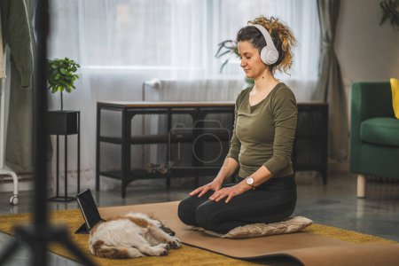 Téléchargez les photos : Une femme adulte caucasien femelle millénium en utilisant des écouteurs pour la méditation guidée en ligne pratiquant le yoga pleine conscience avec les yeux fermés à la maison personnes réelles self care concept copier l'espace - en image libre de droit