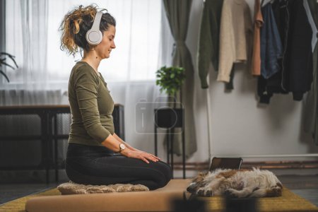 Téléchargez les photos : Une femme adulte caucasien femelle millénium en utilisant des écouteurs pour la méditation guidée en ligne pratiquant le yoga pleine conscience avec les yeux fermés à la maison personnes réelles self care concept copier l'espace - en image libre de droit