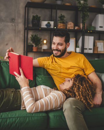 Téléchargez les photos : Homme et femme caucasien adulte couple lire des livres à la maison sur canapé-lit - en image libre de droit
